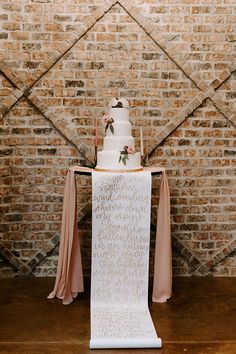 a white wedding cake sitting on top of a wooden table next to a brick wall