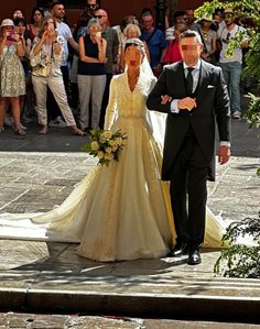 a bride and groom walking down the street in front of a large group of people