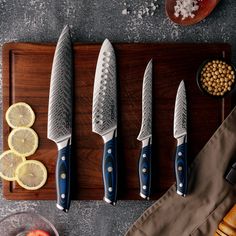 five knives on a cutting board with lemons, tomatoes and other foodstuffs