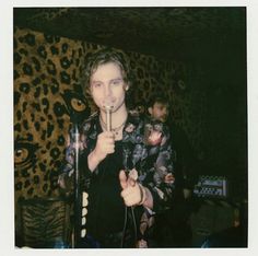 a man standing in front of a leopard print wall holding a microphone and looking at the camera