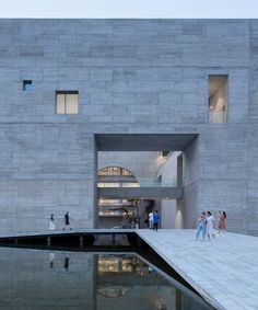 people are walking around in front of a building with a reflecting pool on the ground