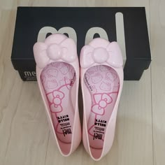 pink hello kitty slippers are sitting on the floor next to a black box with white lettering