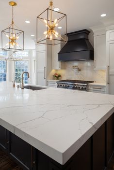 a kitchen with marble counter tops and gold lights hanging from the ceiling over the stove