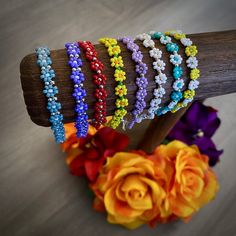 a bunch of bracelets that are on top of a wooden stick next to flowers