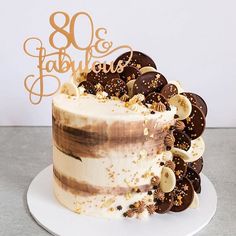 a white cake with chocolate and nuts on top that reads 80 fabulous birthdays written in gold lettering