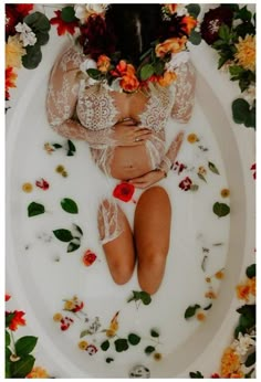 a woman laying in a bath with flowers all around her and wearing a lacy top