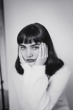 a black and white photo of a woman holding her hands to her face while looking at the camera