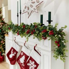 christmas stockings hung on the mantle with holly and red berries hanging from them, along with candles