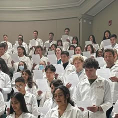 a large group of people in white lab coats holding papers and posing for the camera