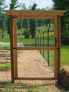 a wooden gate in the middle of a grassy area with hay and trees behind it