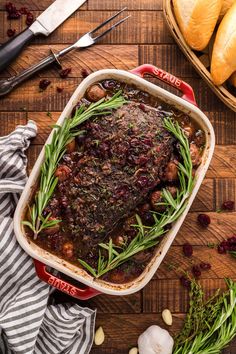 a dish filled with meat and vegetables on top of a wooden table next to bread