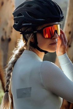 a woman wearing a helmet and sunglasses is standing in front of a tree with her hand on her head