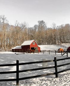 two horses are standing in the snow near a barn and fence, with trees in the background