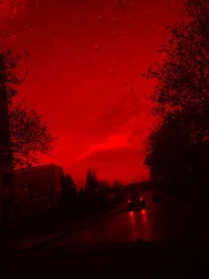 a red sky with rain drops on the ground and trees in the foreground at night