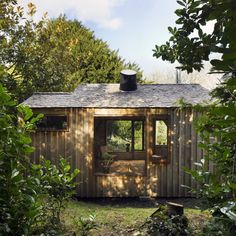 a small wooden shed sitting in the middle of a field with trees and bushes around it