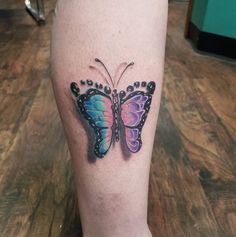 a colorful butterfly tattoo on the left leg and right leg with black dots around it