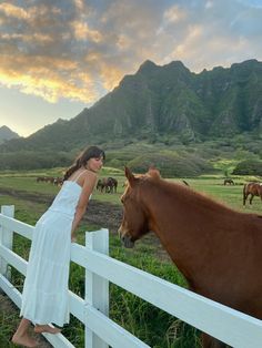 a woman standing next to a brown horse near a white fence