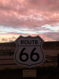 a road sign that reads route 66 in front of a pink sky with clouds behind it