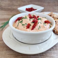 a white bowl filled with dip next to crackers on top of a wooden table