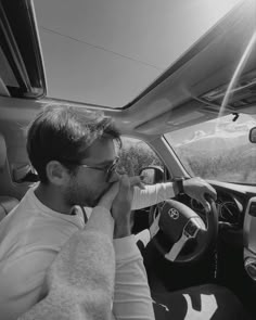 a man sitting in the driver's seat of a car while talking on his cell phone