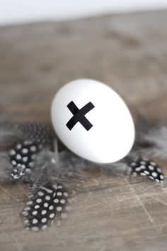 an egg with a cross painted on it sitting next to feathers and eggshells