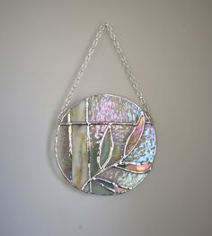 a stained glass piece hanging from a chain on a white wall, with leaves in the center