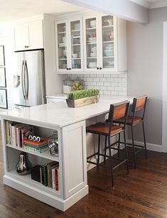 a kitchen with white cabinets and an island that has chairs on it, in the middle of