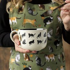 a woman is holding a cup with cats on it and spoon in her hand as she holds