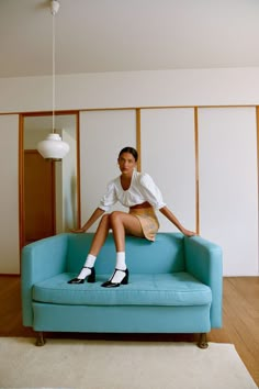 a woman sitting on top of a blue couch next to a white lamp hanging from the ceiling