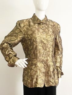 This is a semi sheer metallic blouse by Carlisle, made in Hong Kong.  The bronze background is covered with flowers and leaves that are outlined in gold. The blouse has long cuffs accented with five buttons, closes with seven buttons down the front.  The buttons are round with metallic bits that look like they are floating inside each one.  No size tag, no stretch.  Fits mannequin 35X26X33.  Check measurements.  Content 43 percent silk, 36 percent rayon, 21 percent metallic.  Looks great buttoned or open as a topper.   Measurements taken with blouse laying flat and doubled where appropriate. In order to determine fit we recommend comparing measurements with an item that fits you well. Length 27 inches Shoulder to shoulder 15 inches Sleeve 22 to 25 (folded and not) Underarm to underarm 40 i Gold Fitted Luxury Top, Luxury Fitted Gold Top, Luxury Gold Tops For Evening, Luxury Gold Top For Evening, Luxury Long Sleeve Gold Top, Luxury Gold Long Sleeve Top, Classic Gold Silk Blouse, Classic Gold Formal Blouse, Gold Luxury Blouse For Formal Occasions