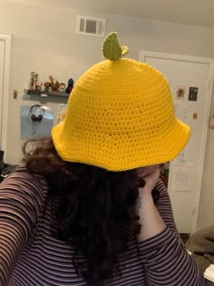 a woman wearing a yellow crocheted hat with a green leaf on it's brim