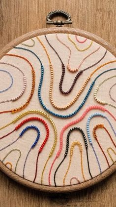 a hand embroidered purse with various colored threads on the front and side, sitting on a wooden surface