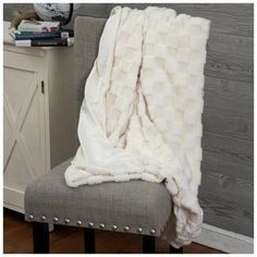 a white blanket sitting on top of a gray chair next to a wooden table and wall