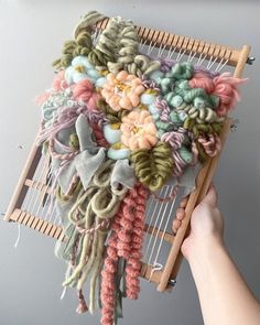 someone is holding up a weaving machine with yarn and flowers hanging from the front end