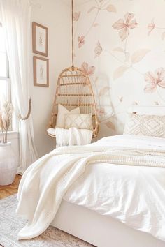 a bed with white sheets and pillows next to a hanging chair in a room that has floral wallpaper on the walls