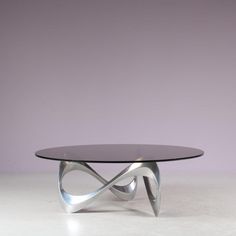 a glass and metal coffee table in front of a purple wall with an abstract design on it