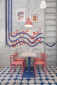 the interior of a restaurant with blue and red lines on the wall, two pink chairs and a white table