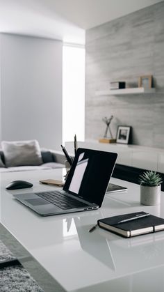 an open laptop computer sitting on top of a white table next to a notebook and pen