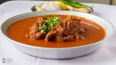 a white bowl filled with meat and garnish on top of a cloth covered table