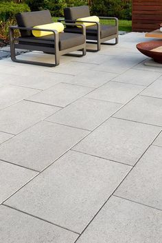 some chairs sitting on top of a cement floor next to a wooden bench and fire pit