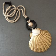 a seashell with a black cord on a gray surface, next to a white bead necklace