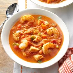 two bowls of soup on a table with spoons and napkins next to it