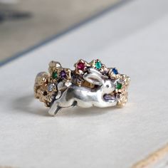 "Our Dearest Bunnikins ring was inspired by both an antique Georgian acrostic love token ring and a beloved Bunnykins bowl my partner grew up with. Spelling out \"DEAREST\" in genuine gemstones across a field of flowers: Diamond, Emerald, Amethyst, Ruby, Emerald, Sapphire, Tsavorite - like an early 19th century acrostic jewel, the first letter of each gemstone name creates the letters. It's a piece that combines the strength and support of sentimental love with the comfort of familiar objects th Heirloom Jewelry With Birthstone For Collectors, Heirloom Birthstone Jewelry For Collectors, Heirloom Sterling Silver Multi-stone Ring, Heirloom Multi-stone Sterling Silver Ring, Acrostic Jewelry, Georgian Engagement Ring, Dreamy Jewelry, Bunny Ring, Rabbit Ring