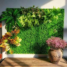 a green wall with plants and flowers on it in front of a wooden table next to a potted plant