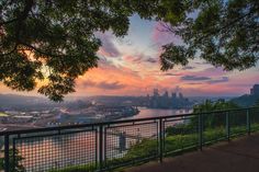 the sun is setting over a city and river as seen from a park bench on top of a hill