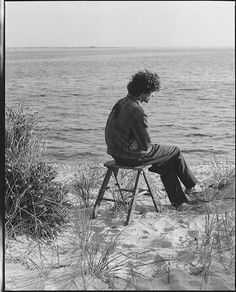 a man sitting on top of a wooden chair near the ocean