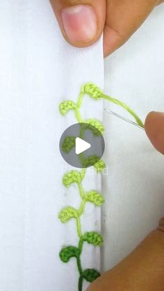 someone is stitching a flower on the side of a piece of white fabric with green thread