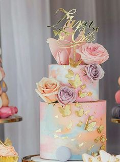 there is a multi layer cake decorated with flowers and butterflies on the table next to cupcakes