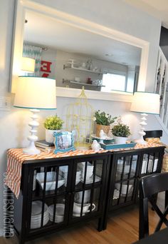 a dining room table with plates and cups on it, next to a lamp that has a birdcage