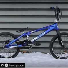 a blue mountain bike parked in front of a garage door with snow on the ground